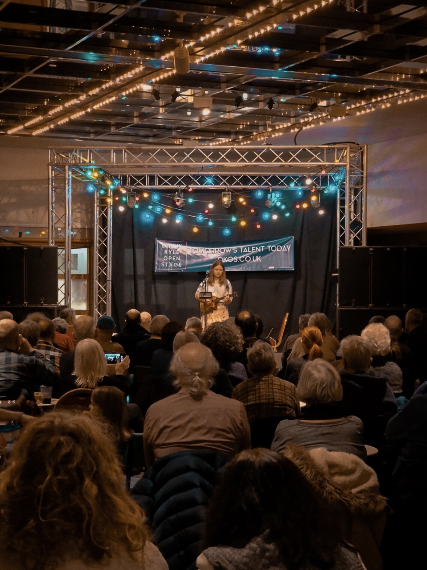 Mila Ziska from afar on a stage playing the ukulele