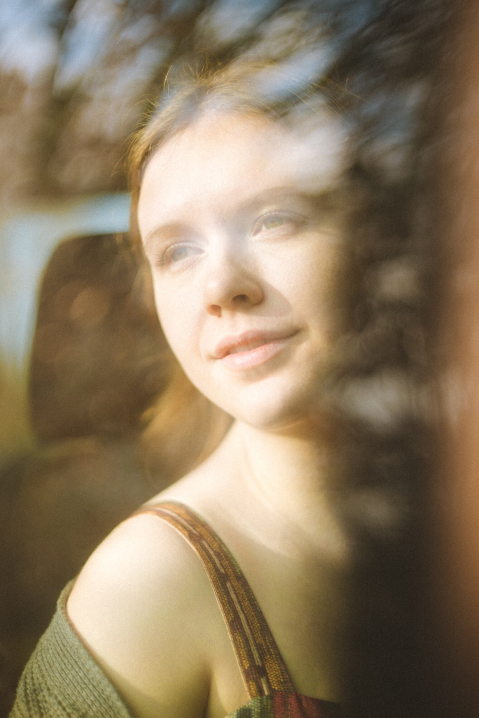 Mila Ziska photographed through a window, trees are reflecting in the glass